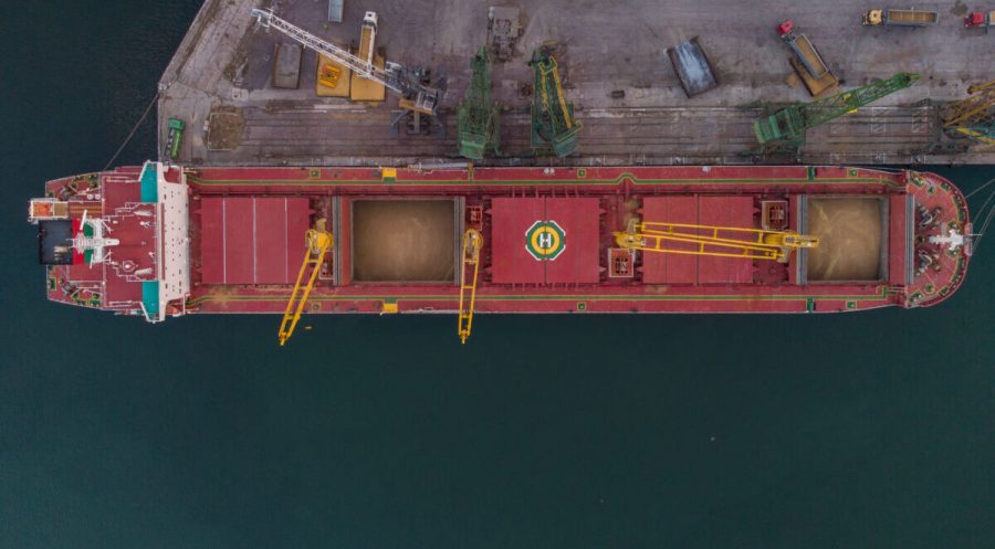 Aerial view of big cargo ship bulk carrier is loaded with grain of wheat in port at sunset