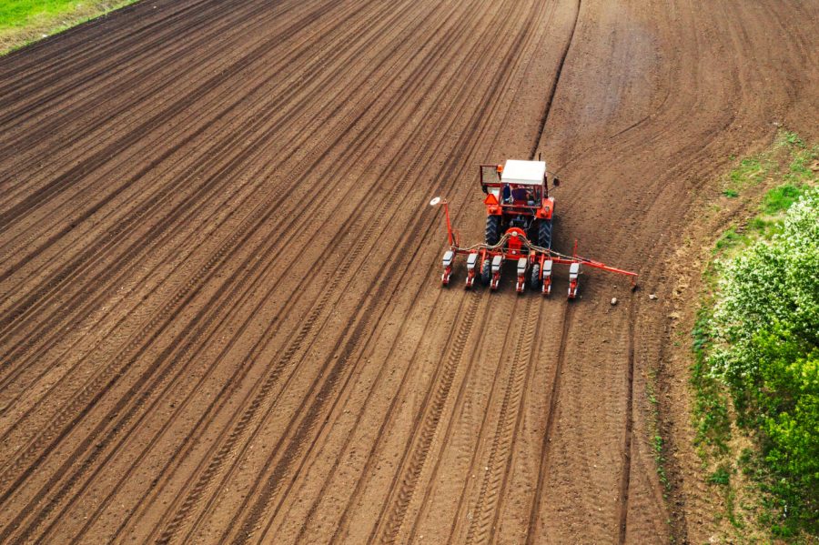 Aerial view of tractor with mounted seeder performing direct seeding of crops on plowed agricultural field. Farmer is using farming machinery for planting process.