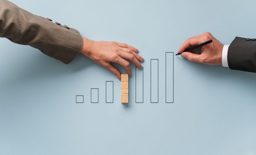 Business partners drawing and building statistical graph of wooden blocks in a conceptual image of economy and financial market.