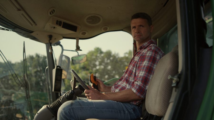 Farmer working tractor cabin at agricultural field. Man observing grain farmland checking modern smart harvesting system. Professional harvester operator driver adjusting machinery on crop season.