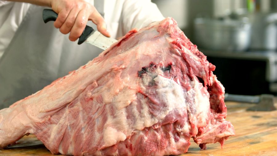 Splitting of pig carcass close up. Butcher cutting up a large slab of raw meat carcass with a knife. Processing a pig at home.